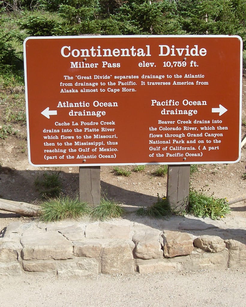 The Irresistible Continental Divide Trail Brown sign at Milner Pass marking the Continental Divide, with arrows showing Atlantic and Pacific Ocean drainage directions and elevation of 10,759 feet.